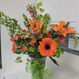 Orange mixed bouquet in a clear glass vase with a green ribbon