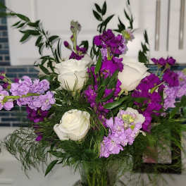White roses and purple flowers arranged in a clear glass vase