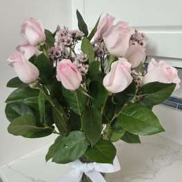Pink roses and small waxflower blooms in a glass vase with a white ribbon.