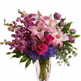 Tall vase of pink lilies, hot pink roses, purple orchids, tulips, and blue hydrangeas.