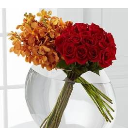 Red roses and orange orchids arranged at an angle in a round clear glass vase