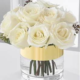 Short arrangement of ivory roses in a clear glass cylinder vase with a wide gold band