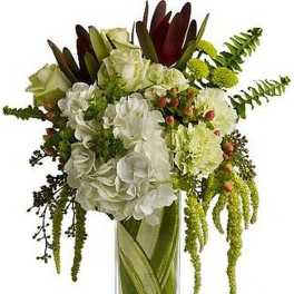 Tall arrangement of white hydrangeas, roses, and green flowers in a clear rectangular glass vase
