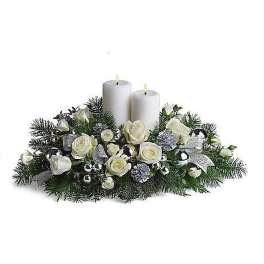 Low centerpiece of white roses and evergreens with two white pillar candles and silver decorations