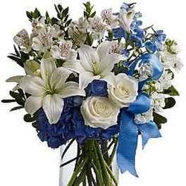 Tall clear vase of white lilies, roses, and blue flowers with a blue ribbon.