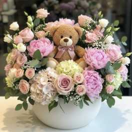 Pink and white floral arrangement with a teddy bear in a white bowl vase