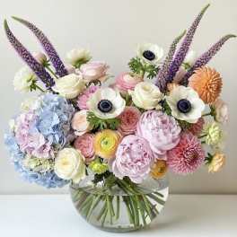 Mixed pastel bouquet in a clear glass vase with purple spikes and white blooms