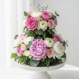 Pink and white roses arranged in a tiered cake shape with a crown topper