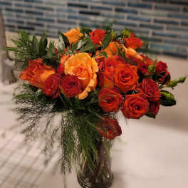 Orange and red roses arranged in a clear glass vase