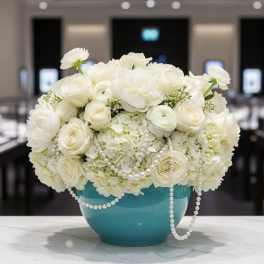 White floral arrangement in a turquoise vase with pearl strands