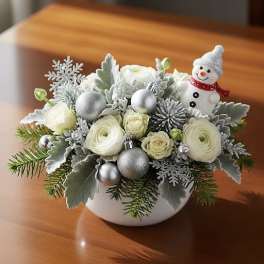 White floral arrangement with a small snowman ornament in a white bowl
