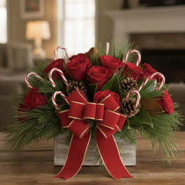 Red roses arranged with candy canes, pinecones, and a large red bow in a wooden box