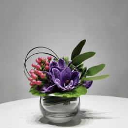Purple orchid arrangement in a clear glass vase with pink berries