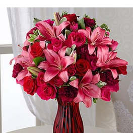 Arrangement of pink lilies and red roses in a red glass vase