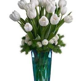 Tall arrangement of white tulips and small white blooms in a blue glass vase