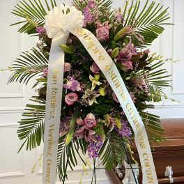 Large funeral wreath with pink and purple flowers and white ribbon on a stand