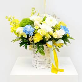 Yellow, white, and blue flower arrangement in a white basket
