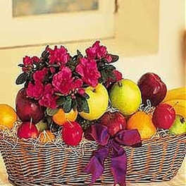 Wicker basket filled with assorted fruit and a pink flowering plant, tied with a purple bow