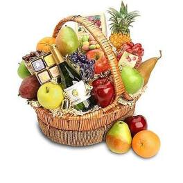 Wicker gift basket filled with assorted fruits, a wine bottle, and gourmet treats