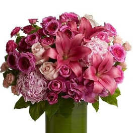 Pink lilies, roses, and hydrangeas arranged in a round bouquet in a green-lined glass cylinder vase