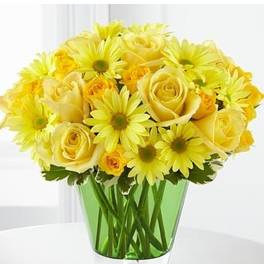 Yellow roses and daisy-style flowers arranged in a clear vase with green glass lining