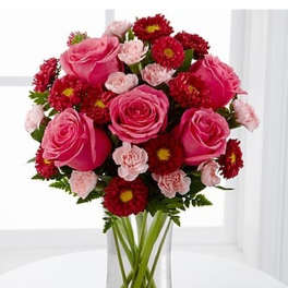 Pink roses with red mums and light pink carnations arranged in a clear glass vase.