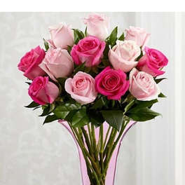 Arrangement of light and dark pink roses in a tall clear vase with pink accents