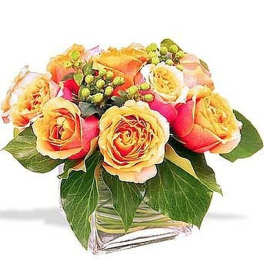 Short arrangement of orange and yellow roses with berries in a clear glass cube vase