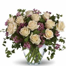 Arrangement of cream roses with small purple flowers and trailing ivy in a clear glass vase