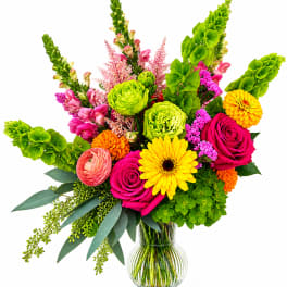 Bright mixed bouquet in a clear glass vase with roses, gerbera daisies, and green blooms