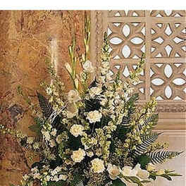 Tall arrangement of white carnations and mixed white flowers in a white ceramic vase