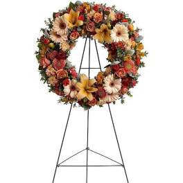 Autumn-toned standing wreath of lilies, roses, and gerbera daisies on a black metal easel