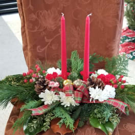 Christmas centerpiece with red candles, white flowers, pinecones, and plaid ribbon