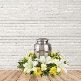 White lilies and yellow flowers arranged around a silver urn