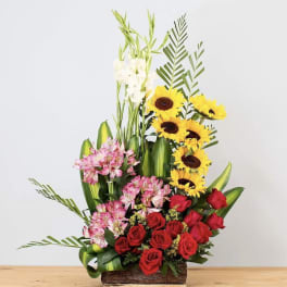 Tall mixed flower arrangement with red roses, pink alstroemeria, and sunflowers