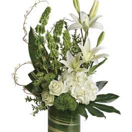 Tall arrangement of white lilies, roses, and hydrangeas with green accents in a clear glass cylinder vase