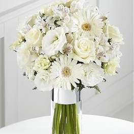 Tall arrangement of white gerbera daisies, roses, and mixed blooms in a clear glass vase.