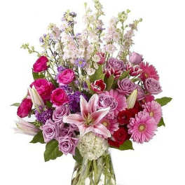 Mixed bouquet of pink lilies, roses, gerberas, and purple blooms in a clear glass vase