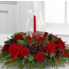 Low centerpiece of red roses and carnations with pinecones around a red candle in a glass hurricane.