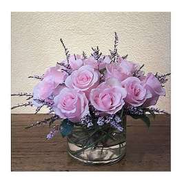 Short arrangement of light pink roses with purple filler in a glass vase