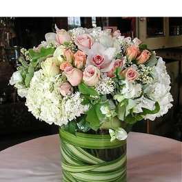 Round arrangement of white hydrangeas and pale pink roses in a clear vase lined with green leaves
