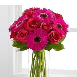 Bright pink gerbera daisies and red roses in a tall rectangular glass vase