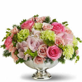 Low arrangement of pink roses, green carnations, and pale hydrangeas in a silver pedestal bowl