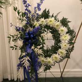 White chrysanthemum wreath with blue flowers and ribbon on a stand