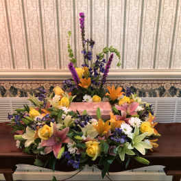 Large floral casket spray with lilies, roses, and purple accents