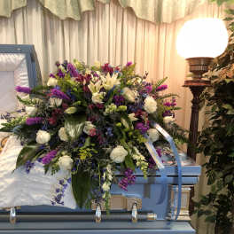 Large floral casket spray with white roses, lilies, and purple accents