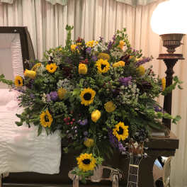 Large floral spray with yellow sunflowers and purple accents on a casket