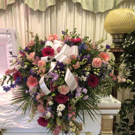 Large pink and purple funeral spray on a white casket with ribbon