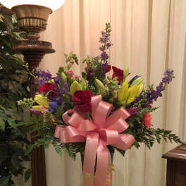 Colorful bouquet of roses, lilies, and purple flowers in a glass vase with a pink bow