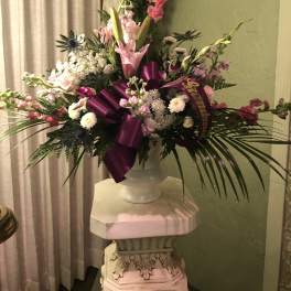 Large pink and white floral arrangement in a white vase with a purple ribbon